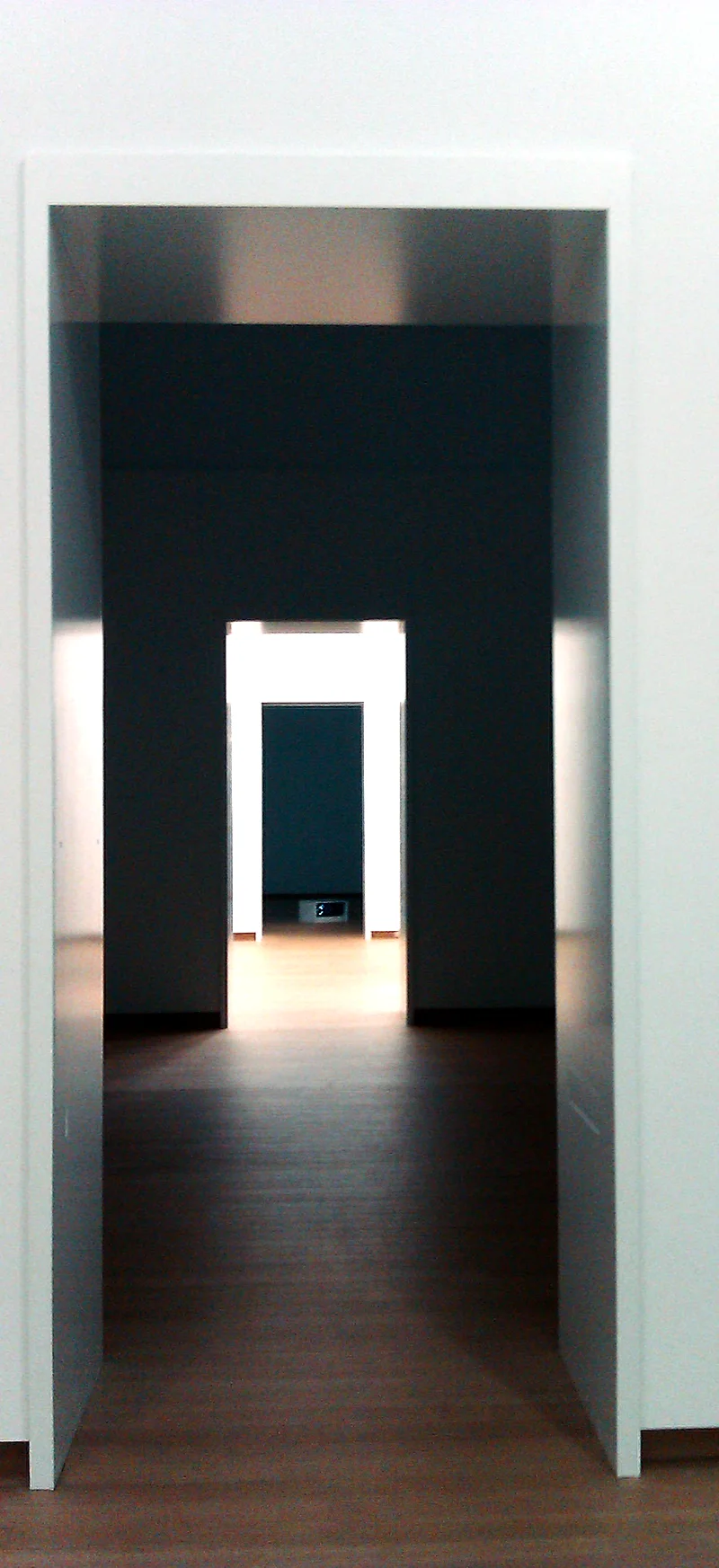 A doorway through a white wall into a lit room beyond.