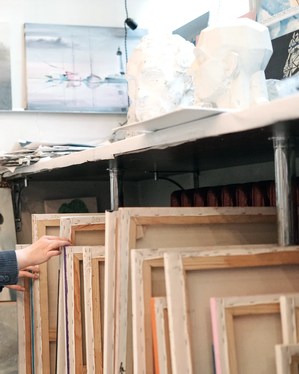 Stretchers stacked against a studio wall, a hand pulling one forward.
