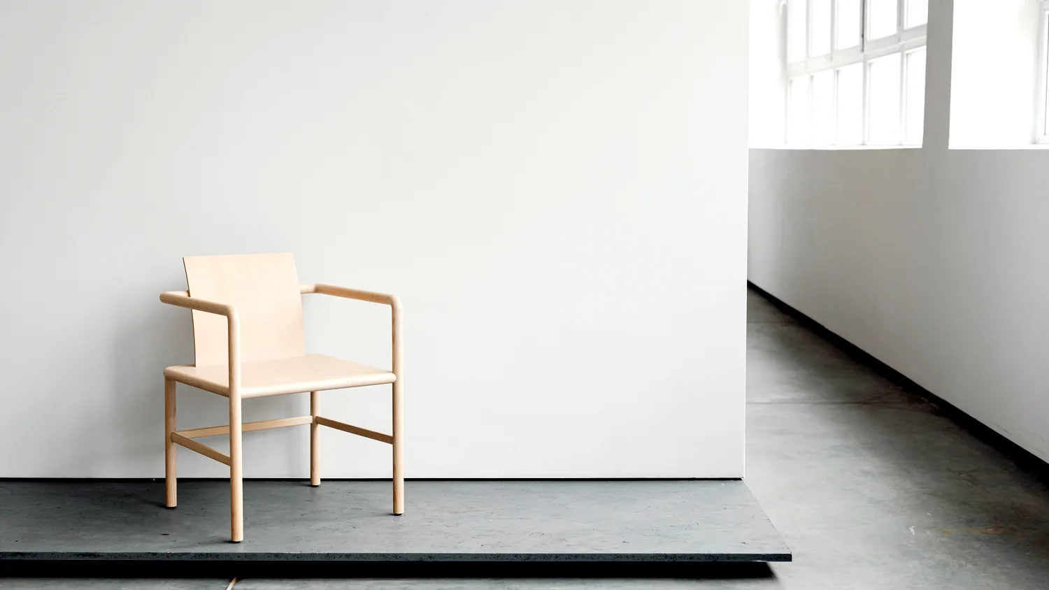 An empty white room with one chair standing on a low plinth beside a bare wall.